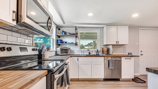 Una cocina moderna con armarios blancos, una estufa de acero inoxidable y una encimera de madera.