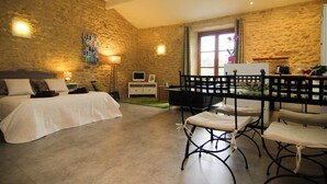Ein Schlafzimmer mit Steinwand, einem Bett, einem Schreibtisch mit Stuhl, einem Fernseher und einem Fenster mit Vorhängen.