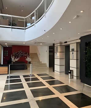 Experience the sleek, open design of our lobby, featuring a central staircase, minimalist reception area, and elegant decorative touches.