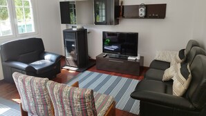 Ein Wohnzimmer mit einer Couch, einem Sessel, einem Fernseher, einem Kamin und einem Fenster.