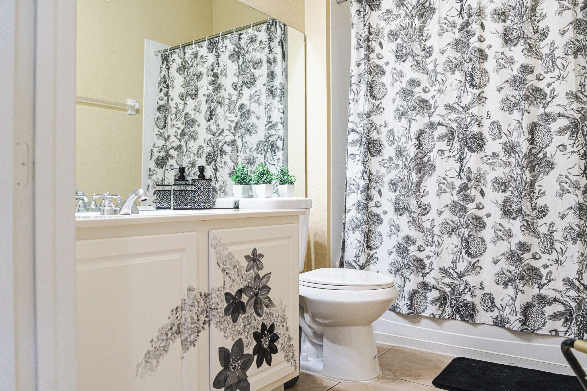 A bathroom with a toilet, a sink with a mirror, and a shower curtain with a floral pattern.