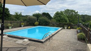A rectangular swimming pool with a tiled deck, surrounded by a wooden fence and various potted plants. - La Petite Maison, charming 3 bedroom Gite in Saint-Estephe, 24360, Dordogne, (Saint-Estèphe)