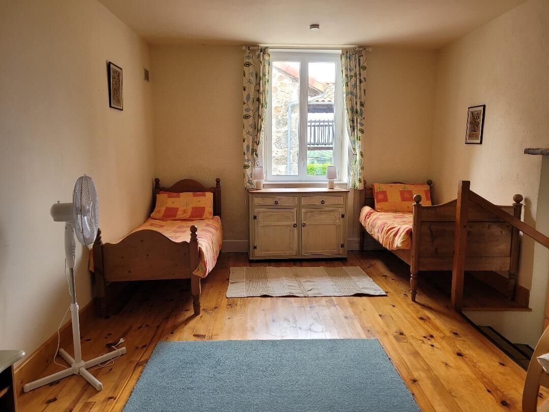 Un dormitorio con dos camas de madera, una ventana con cortinas, un ventilador y una escalera de madera.
