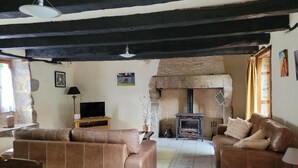 A cozy living room with two brown leather sofas, a television, a fireplace, and a stone wall. - La Petite Maison, charming 3 bedroom Gite in Saint-Estephe, 24360, Dordogne, (Saint-Estèphe)