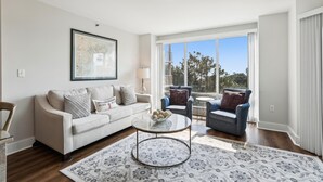 A living room with a white sofa, two armchairs, a coffee table, and a large window with a view of trees. - Modern 4th Floor Villa w/ Private Balcony (Hilton Head Island)