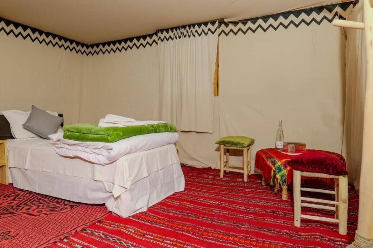 A room with a bed, a small table, a chair, and a red patterned rug.