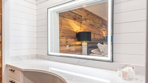 A bathroom with a white marble countertop, a wooden wall, a black lamp, and a glass container with cotton balls.