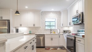 A modern kitchen with white cabinets, stainless steel appliances, and a large window providing natural light.