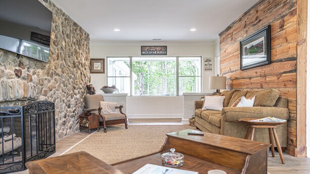 A living room with a stone wall, a wooden wall, a fireplace, a sofa, a coffee table, and a window with a view of trees.