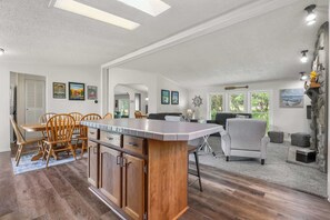 A spacious living area with a kitchen island, dining table, and chairs. There are framed pictures on the walls, a large window, and a stone accent wall. - The Sweet Retreat: Newly Remodeled Sturgeon Bay Ho (Sturgeon Bay)