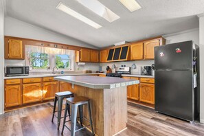 A kitchen with wooden cabinets, a black refrigerator, a microwave, and a large island with stools. - The Sweet Retreat: Newly Remodeled Sturgeon Bay Ho (Sturgeon Bay)