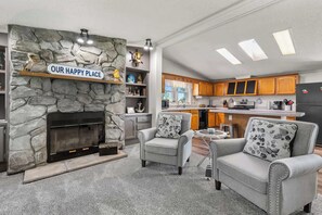 A cozy living room with a stone fireplace, two armchairs, a coffee table, and a kitchen in the background. - The Sweet Retreat: Newly Remodeled Sturgeon Bay Ho (Sturgeon Bay)