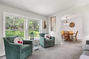 A room with two green armchairs, a wooden dining table with chairs, a chandelier, and a clock on the wall. - The Sweet Retreat: Newly Remodeled Sturgeon Bay Ho (Sturgeon Bay)