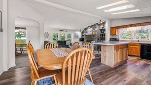 Une cuisine spacieuse dotée d’un îlot central, d’une table à manger en bois avec des chaises, et offrant une vue sur l’extérieur grâce à de grandes fenêtres.
