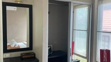 Habitación de hotel con cama, escritorio con silla, espejo, armario, ventana y teléfono.