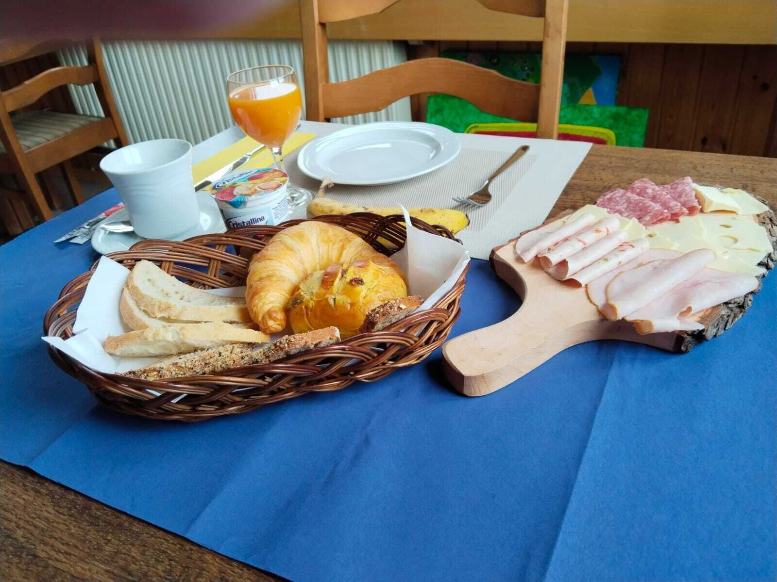 Ein Frühstücksteller mit Brot, Croissant, Schinken, Käse und einem Glas Orangensaft auf einem Tisch.