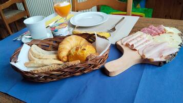 Ein Frühstücksteller mit Brot, Croissant, Schinken, Käse und einem Glas Orangensaft auf einem Tisch.