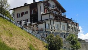 A two-story hotel with a balcony on the upper floor, situated on a hillside with a clear sky. - Hotel Rhoneblick (Guttet-Feschel)