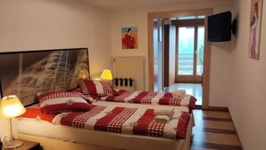 A hotel room with a bed, a nightstand, a lamp, a painting, a television, and a view of the outside. - Hotel Rhoneblick (Guttet-Feschel)