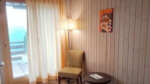 A room with a wooden floor, a chair, a small table, a lamp, and a painting on the wall. - Hotel Rhoneblick (Guttet-Feschel)