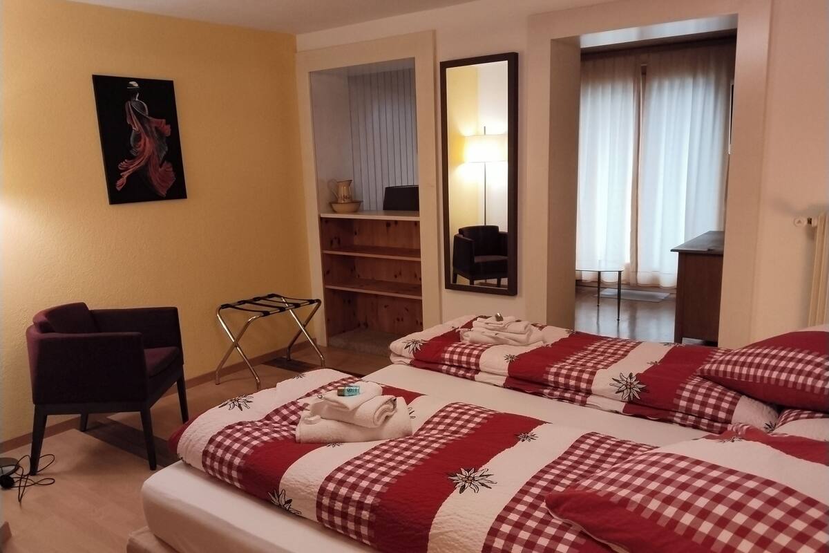 Hotellihuoneessa on kaksi sänkyä, tuoli, pieni pöytä, peili ja taulu seinällä.