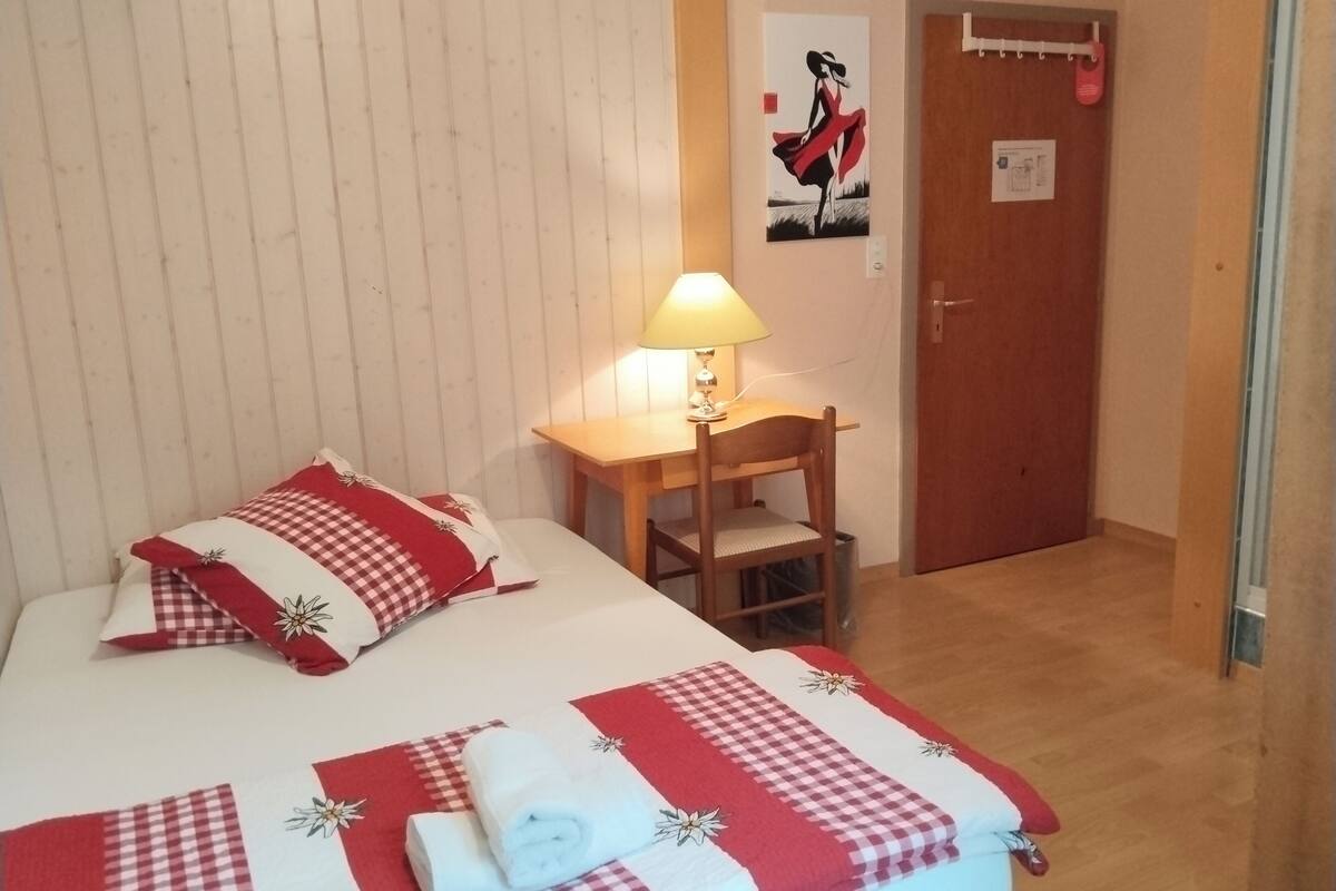 Hotellihuone, jossa on sänky, työpöytä, tuoli, lamppu ja ovi.