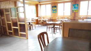 A spacious dining area with wooden tables and chairs, large windows with curtains, and a tiled floor. - Hotel Rhoneblick (Guttet-Feschel)