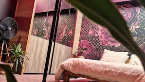 A bedroom with a bed, a fan, a potted plant, and a wall with a floral design. - AKA LOVE ROOM (Lavaur)