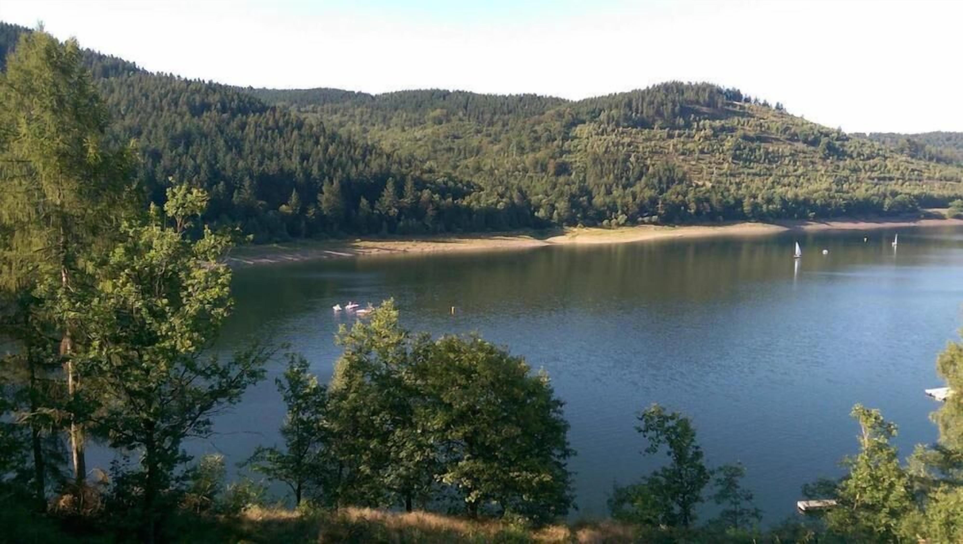 Un lac entouré de collines boisées, avec des bateaux sur l’eau.