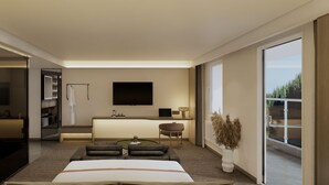 Habitación de hotel moderna con una cama grande, una zona de estar con una mesa de centro, un televisor montado en la pared, un baño con puerta de vidrio y vistas al exterior.