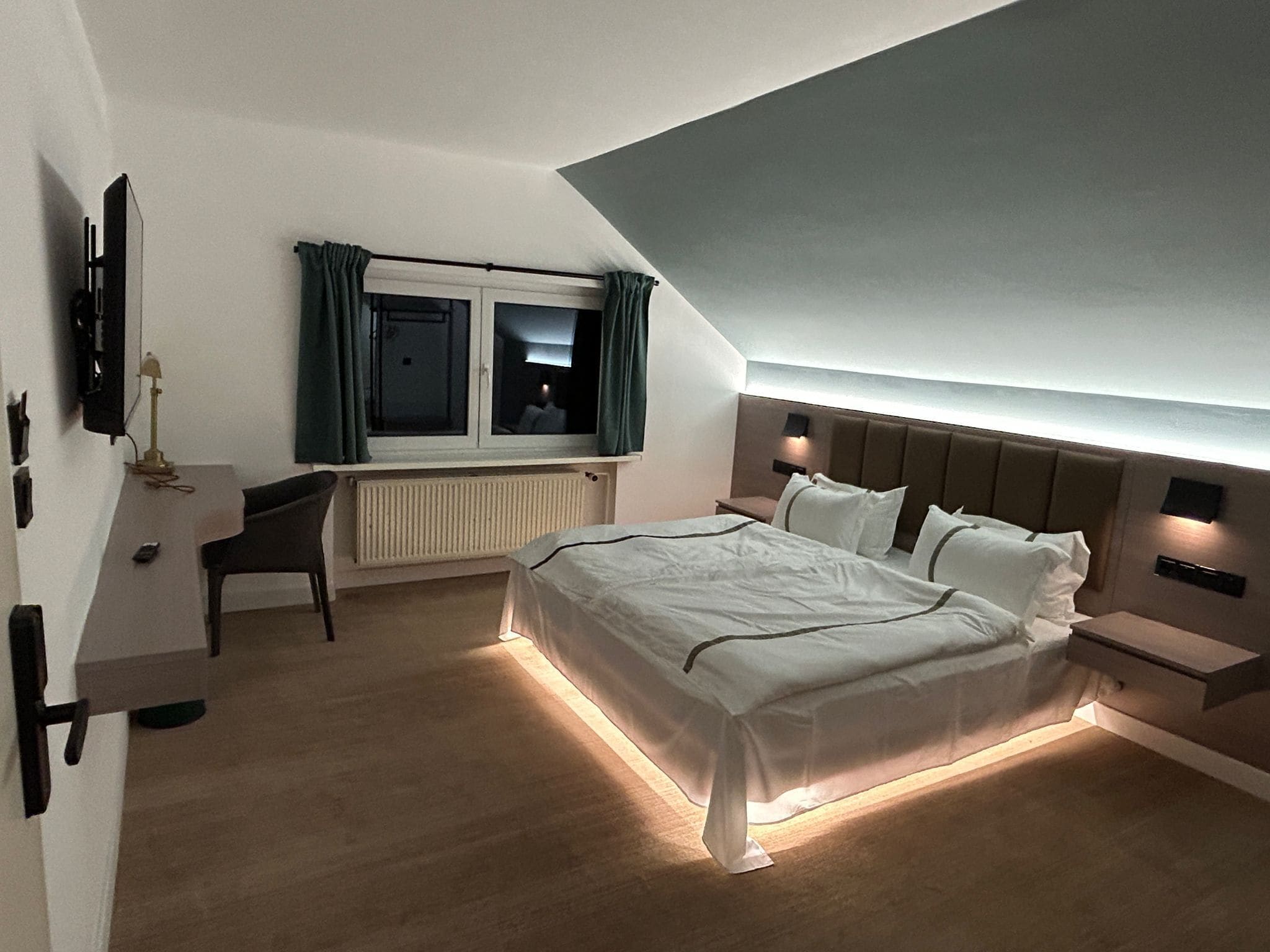 Une chambre moderne avec un grand lit, des tables de chevet, un bureau et une fenêtre avec des rideaux.