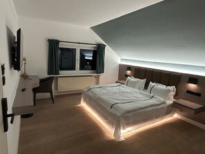 Un dormitorio moderno con una cama grande, mesitas de noche, un escritorio y una ventana con cortinas.