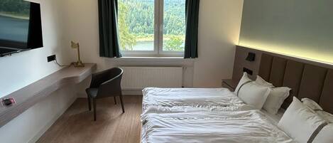 Una camera d'albergo con due letti, una scrivania, una sedia, una televisione e una finestra con tende.