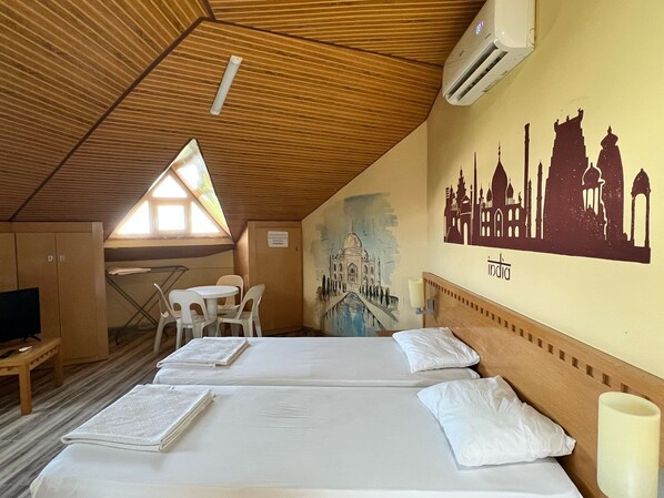 A hotel room with two beds, a small table, chairs, and a mural of Indian landmarks. - Esma Apart Otel (Alanya)