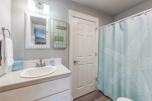 A bathroom with a white sink, a mirror, a towel rack, a door, and a shower curtain. - Beach Daze- Roomy1 BDRM a block from the BEACH & Large Pool (Port Aransas)