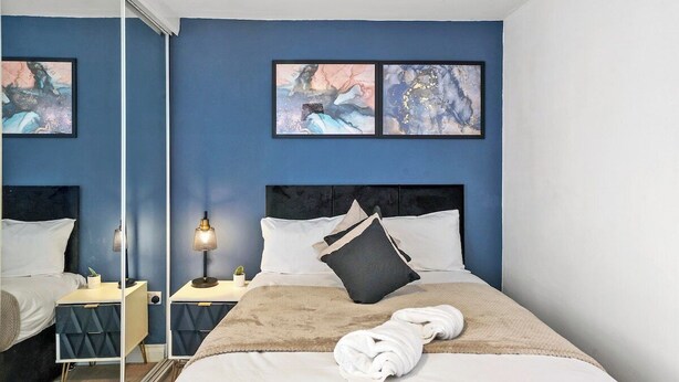 A hotel room with a bed, bedside tables, a lamp, artwork on the wall, and a mirror.