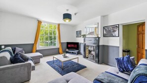 A modern living room with a gray sofa, a blue rug, a fireplace, and a television displaying 'NETFLIX'.