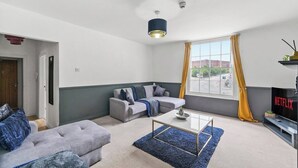 A modern living room with a grey sofa, a blue rug, and a TV displaying 'NETFLIX'.