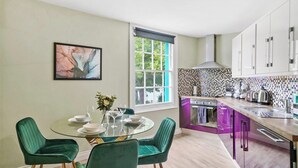 A modern kitchen with a purple cabinet, a glass dining table with chairs, and a window with a view of greenery.