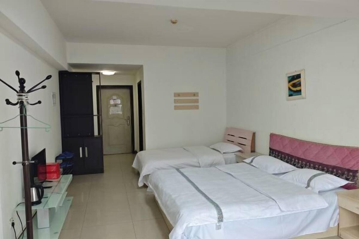 Une chambre d’hôtel avec deux lits, une armoire, un porte-manteau et un petit bureau.