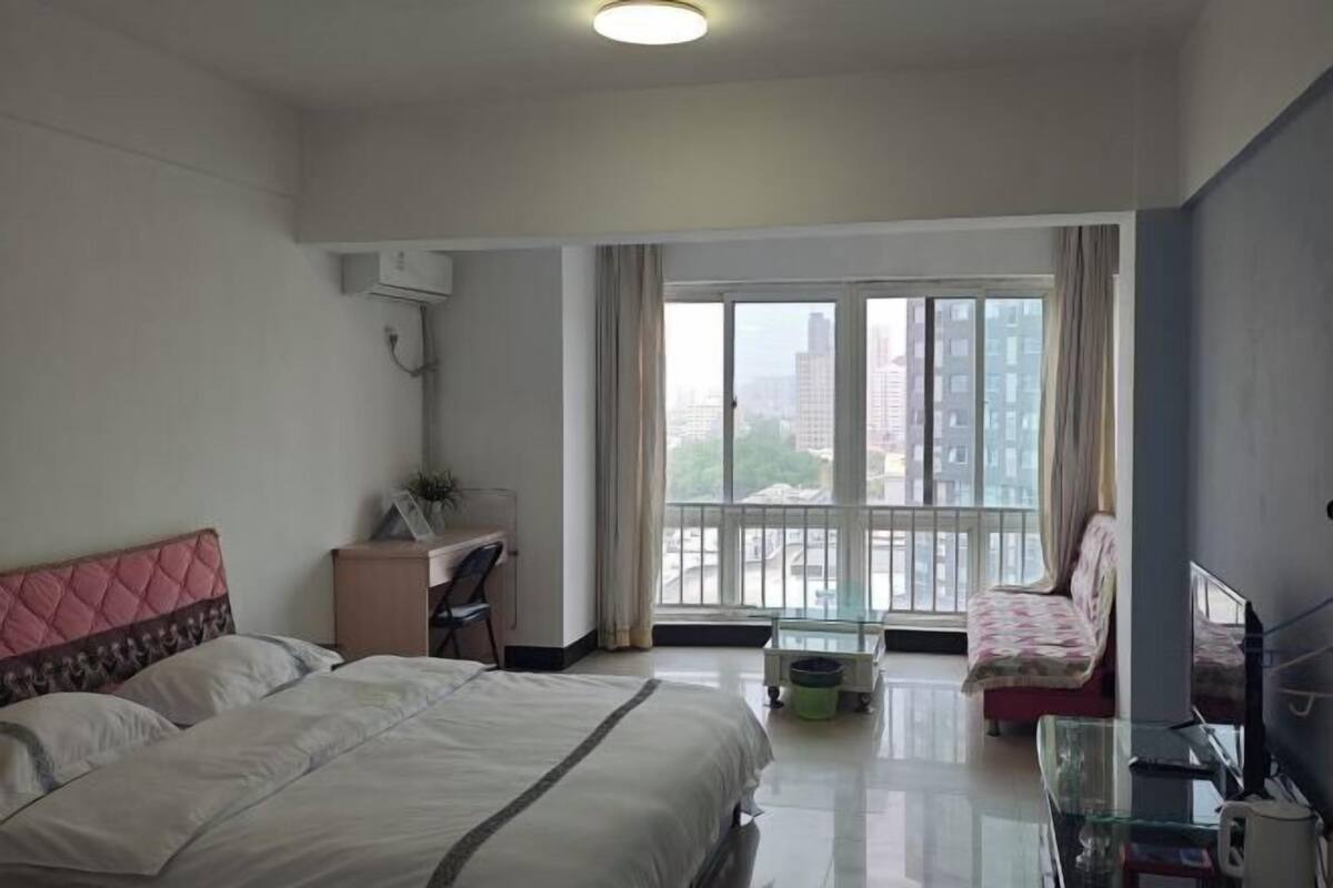 Une chambre d’hôtel équipée d’un lit, d’un bureau, d’une chaise, d’une télévision et d’un balcon donnant sur des immeubles.