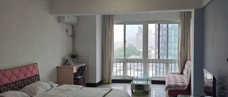 Een hotelkamer met een bed, een bureau, een stoel, een televisie en een balkon met uitzicht op gebouwen.