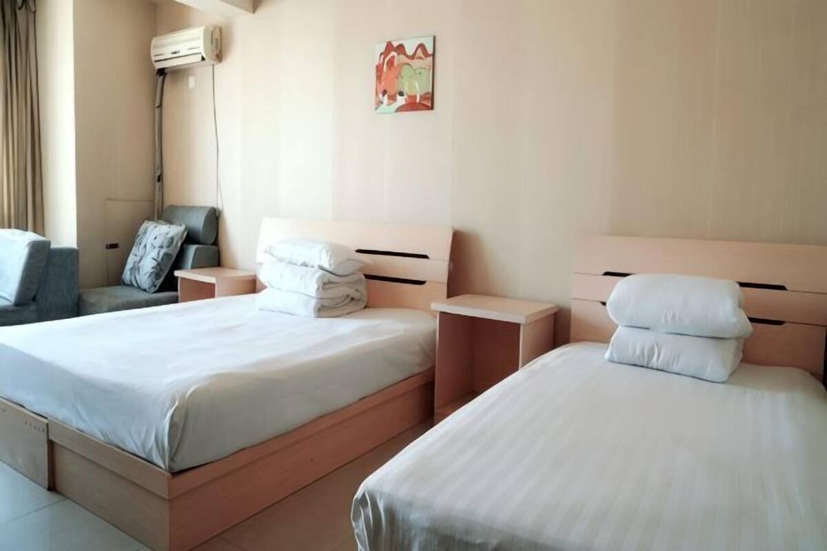 Une chambre d’hôtel avec deux lits, un canapé, un climatiseur fixé au mur et un tableau.