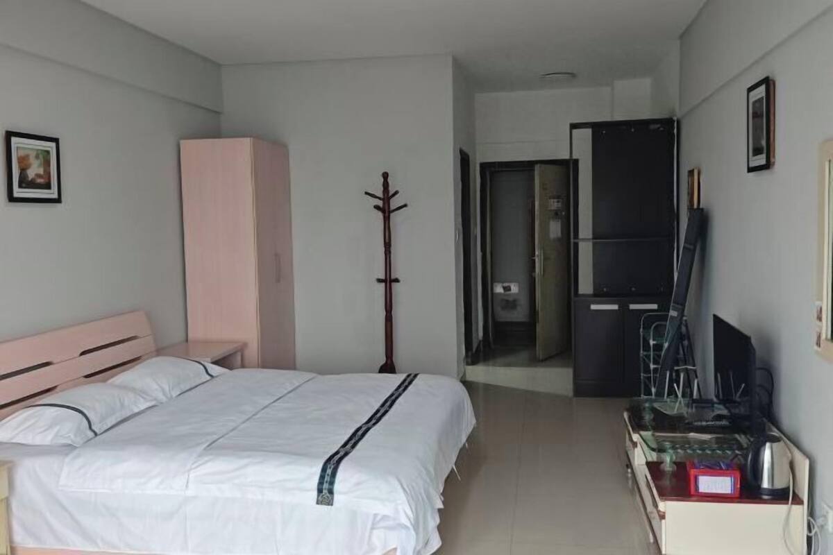 Une chambre à coucher comprenant un lit, une armoire, un porte-manteau et un bureau avec un ordinateur et une bouilloire.