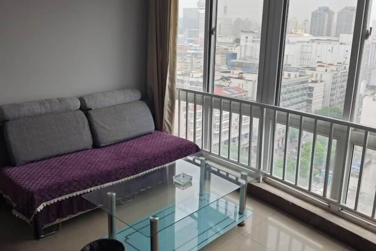 Une pièce avec un canapé, une table basse en verre et une vue sur les immeubles, grâce à de grandes fenêtres.