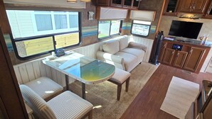 Interior compacto de una autocaravana con kitchenette, zona de comedor y área de descanso con sofá y sillones.