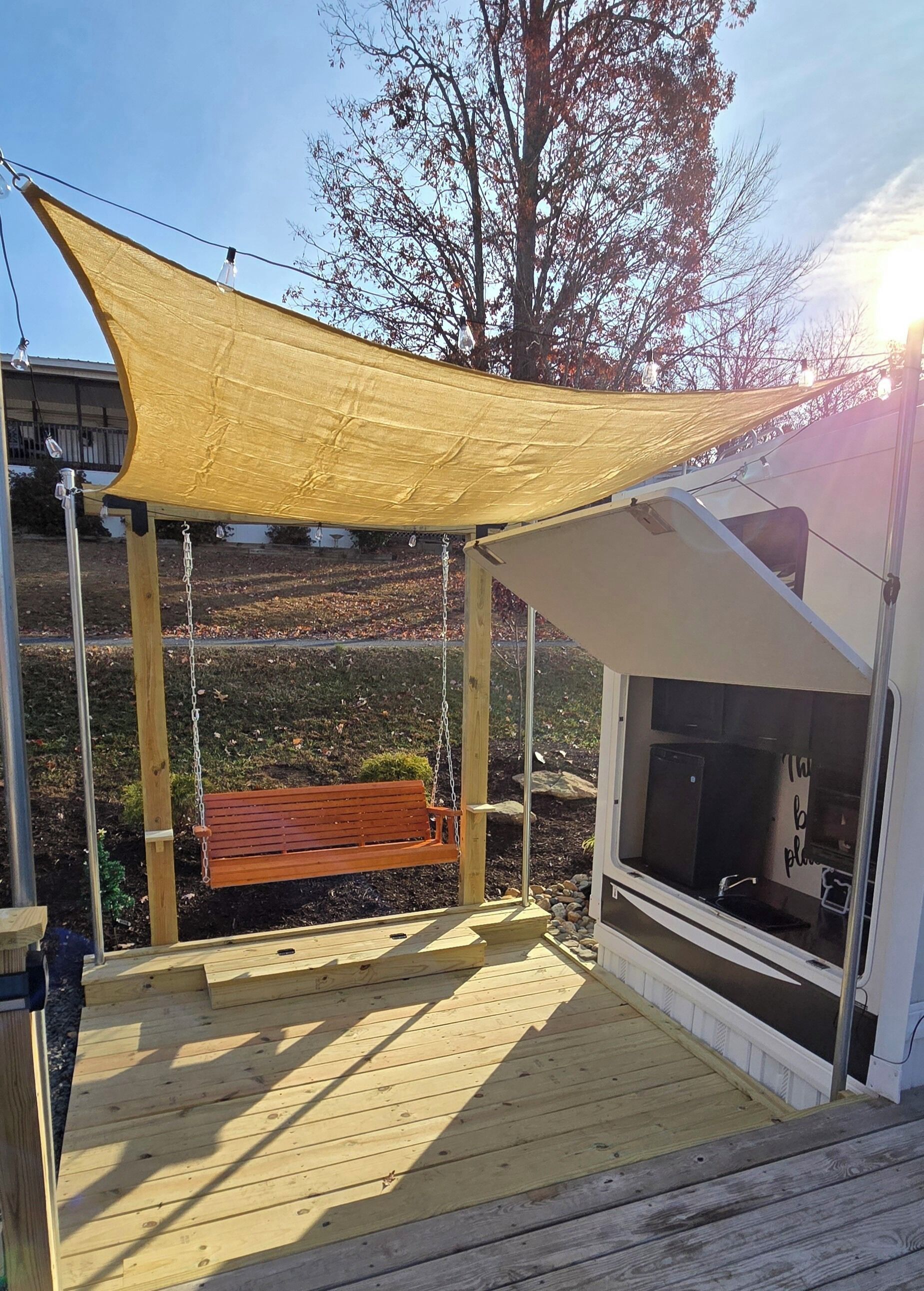 Une terrasse en bois avec une balançoire, un auvent et une fenêtre avec un évier.