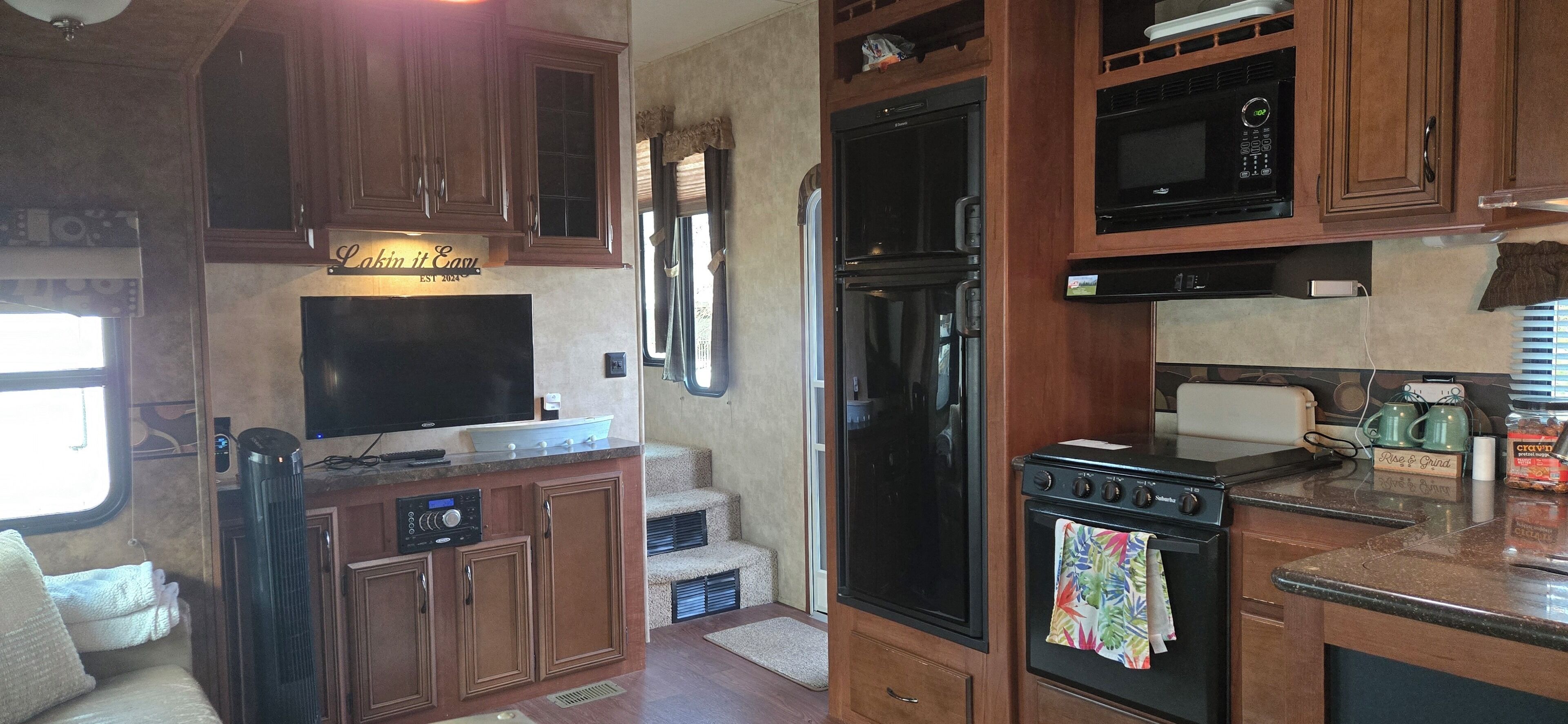 A kitchen with wooden cabinets, a built-in oven, a microwave, and a large flat-screen TV.
