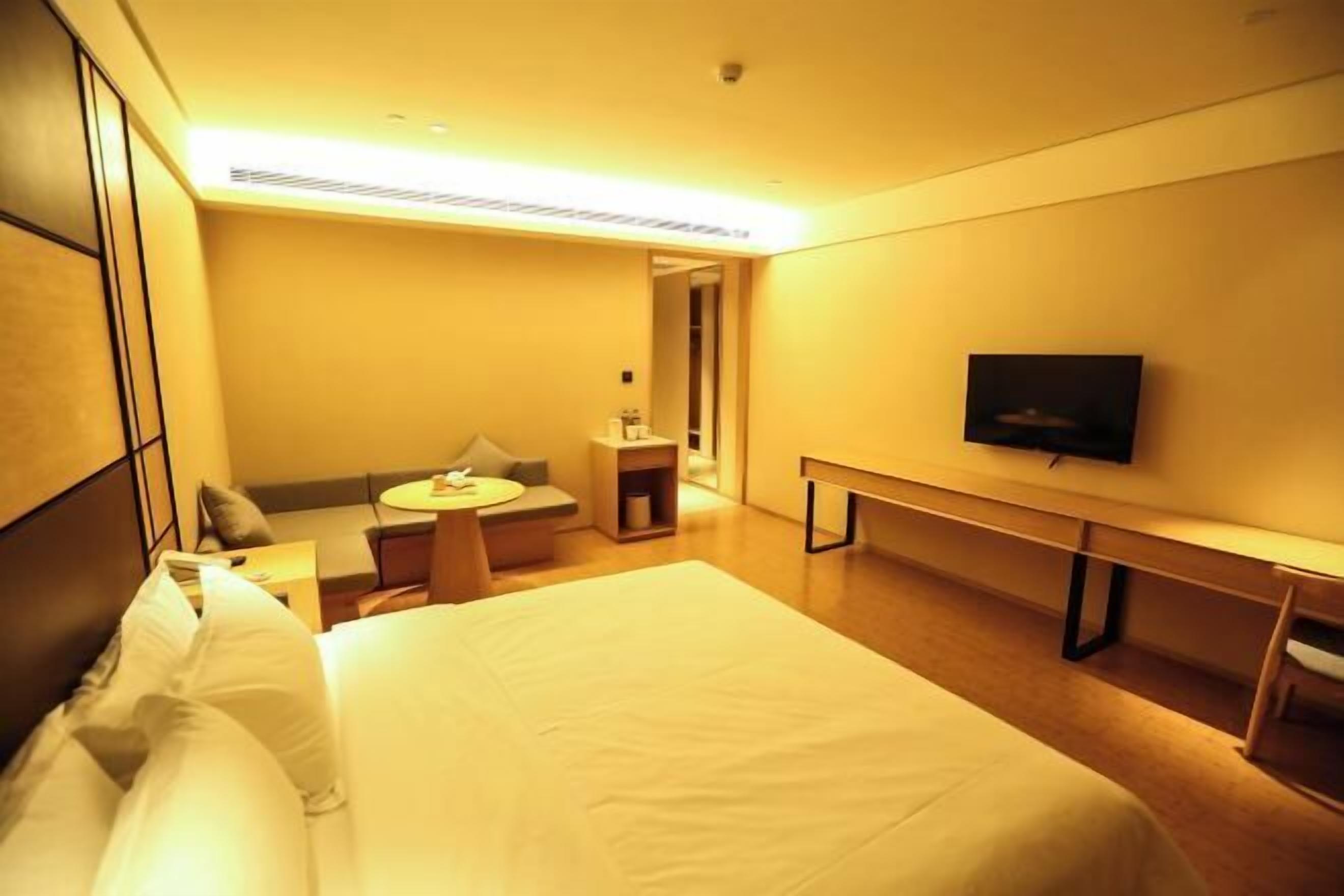 A hotel room with a large bed, a desk, a chair, a TV, and a small seating area with a sofa and a table.