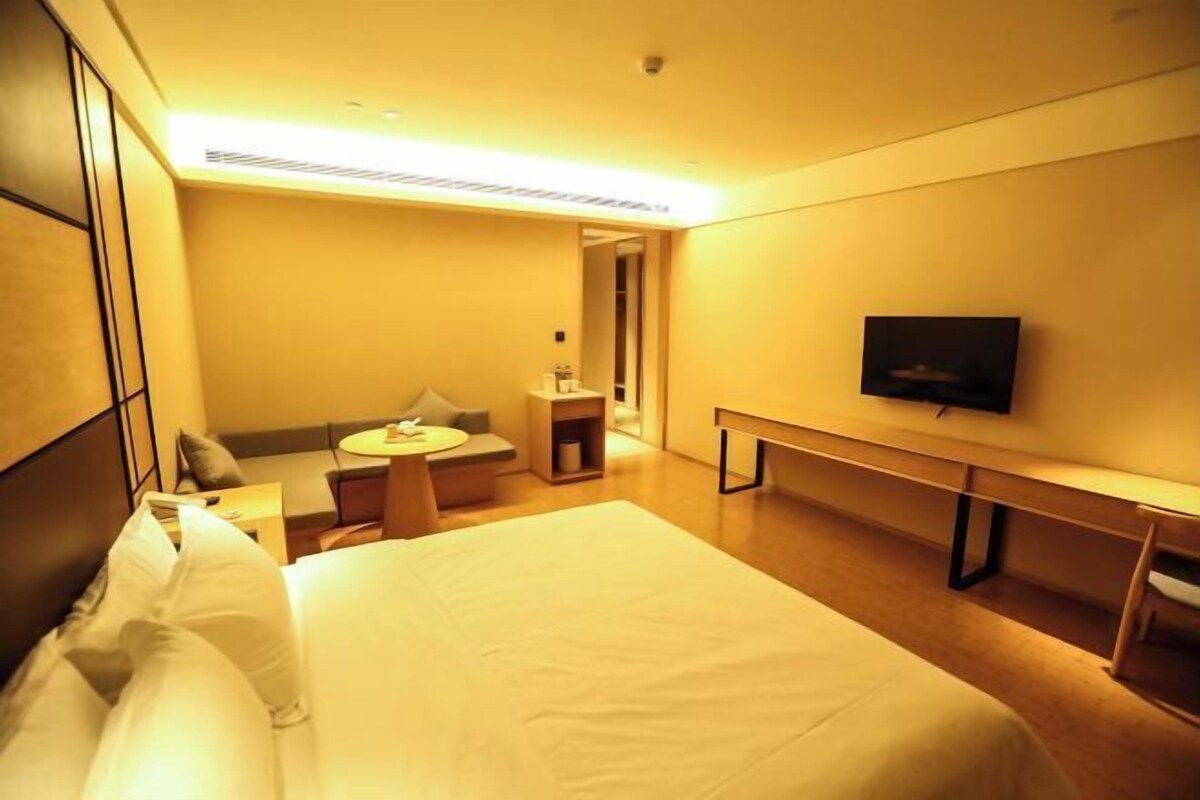 A hotel room with a large bed, a desk, a chair, a TV, and a small seating area with a sofa and a table.
